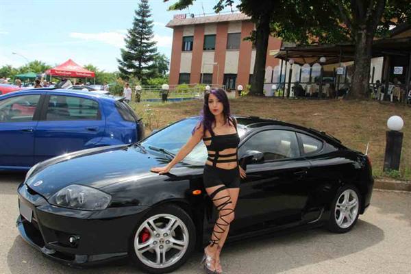 Purple-haired woman leaning on a black Hyundai Coupé at a car meet