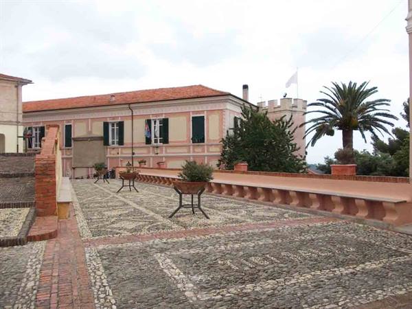 Pebble terrace in front of pink building with tiled roof, palms and grey sky