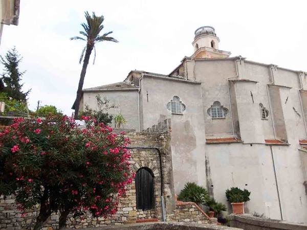White church with bell tower, blooming oleander, palm tree and stone walls