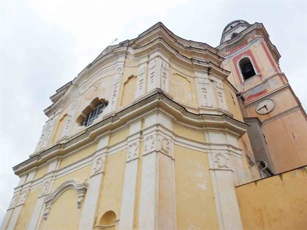 Yellow baroque church with ochre bell tower and clock, grey sky