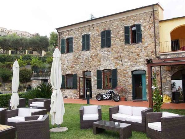 Motorcycle parked before a stone house with closed umbrellas and wicker sofas
