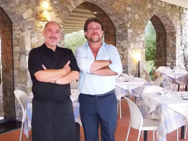 Two men with crossed arms in a stone-arched restaurant with set tables