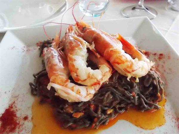 White plate with squid ink spaghetti topped with large prawns, natural light