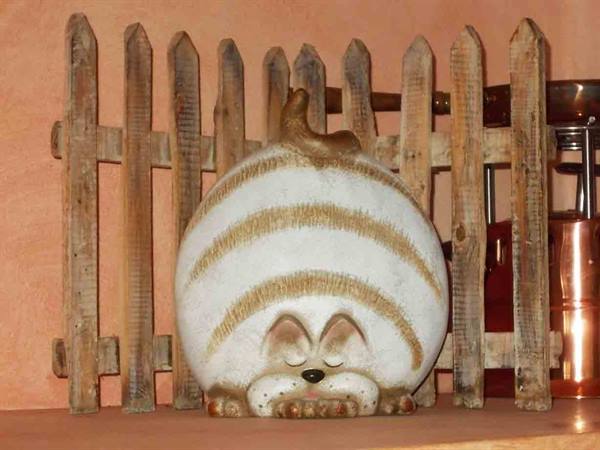 Ceramic statue of a sleeping cat in front of a wooden picket fence