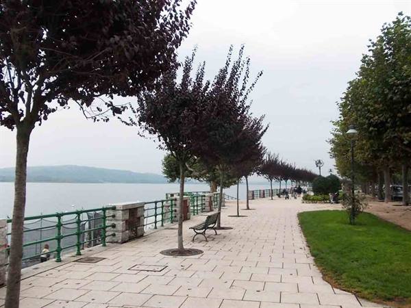 Lakeside promenade with benches, green railings and trees, people strolling