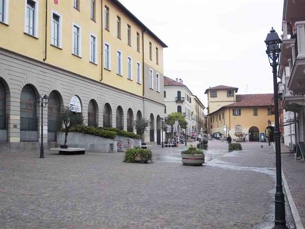 Cobbled square with arcaded yellow buildings, planters and lampposts under grey sky