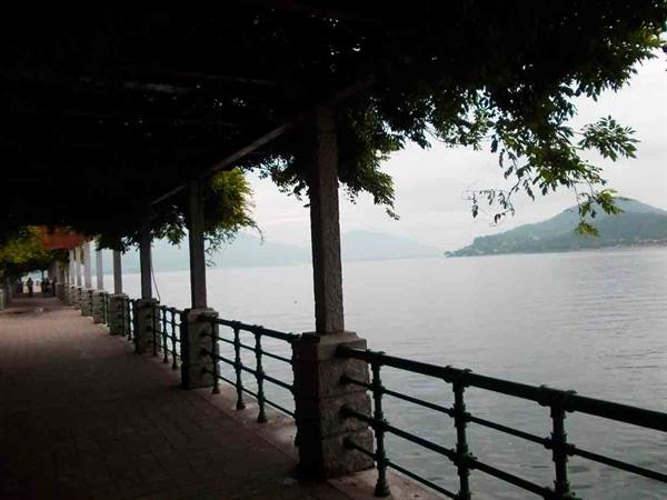 Covered lakeside walkway with stone pillars and green iron railing