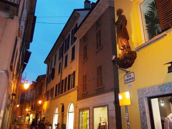 Illuminated wooden statue on yellow facade at Via Cavour at dusk