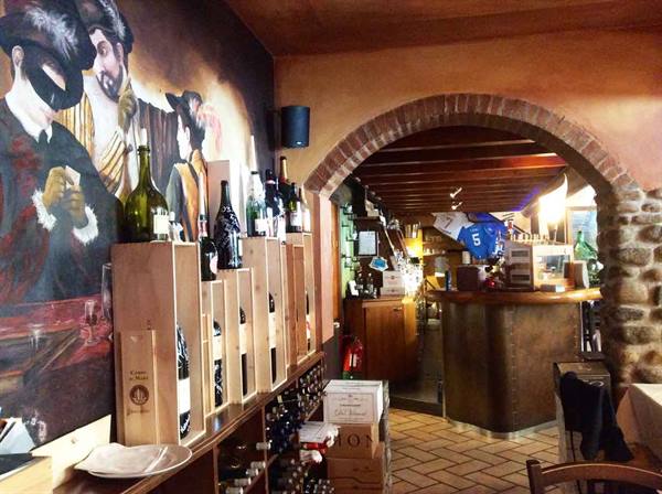 Wine bottles in wooden crates under a mural, brick archway toward the bar