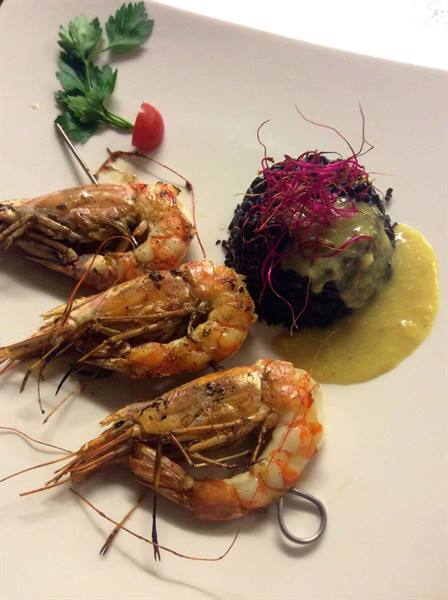 Grilled prawns on skewer with cuttlefish ink rice and yellow sauce