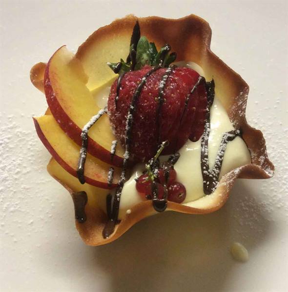 Crispy pastry basket with cream, strawberry, peach slices and chocolate drizzle