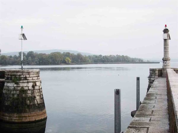 Stone pier with signal lighthouse on the lake, red and green lights, cloudy day