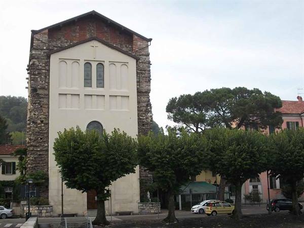 Stone and white plaster church facade with trees and cars in a square