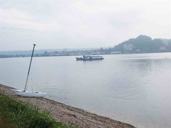 Ferry crossing misty lake, small sailboat beached on pebbly shore