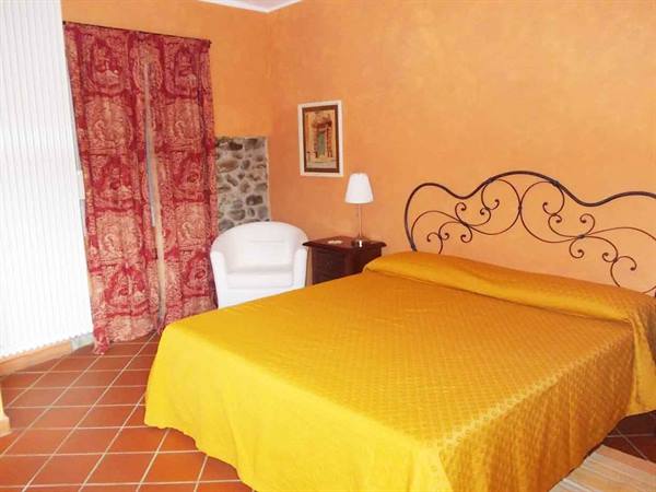 Bedroom with double bed covered in yellow, wrought iron headboard, orange walls