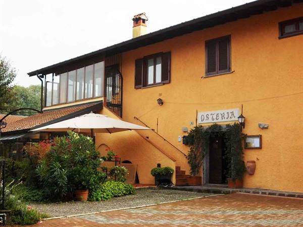 Ochre osteria facade with parasol, potted plants and greenery-framed entrance