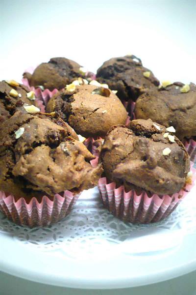 Chocolate muffins topped with nuts in pink cases on white plate