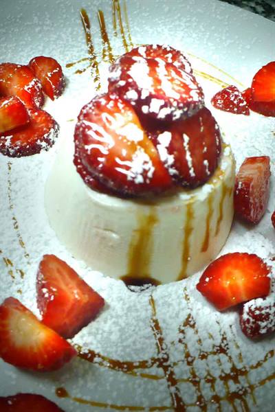Panna cotta topped with fresh strawberries, powdered sugar and caramel drizzle