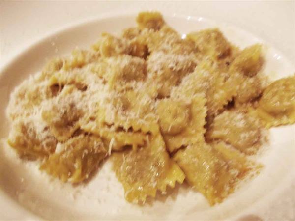 White plate of meat ravioli topped with grated cheese, warm light