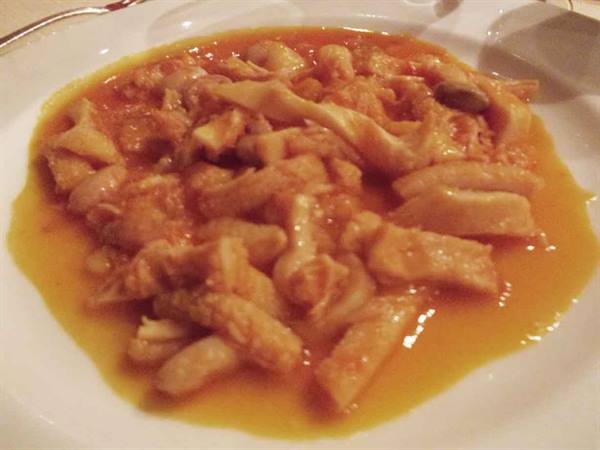 Tripe in tomato sauce served on a white plate at the table