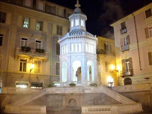 Illuminated marble kiosk at night among buildings, yellow lamps and white staircase