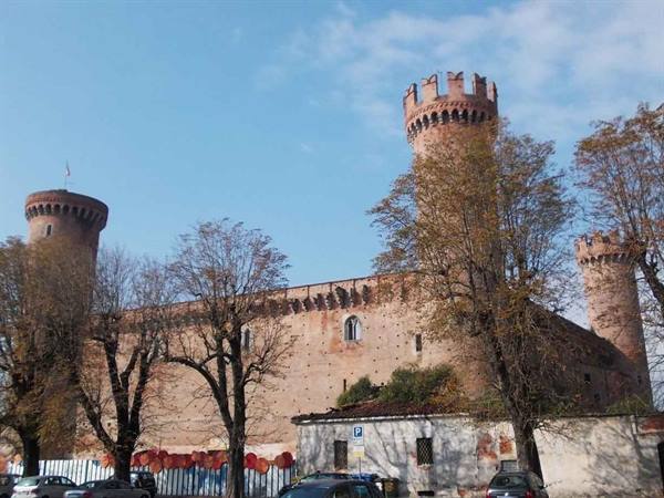 Ivrea Castle, brick towers with battlements among autumn trees and parked cars