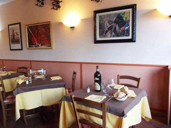 Trattoria dining room with set tables, yellow tablecloths, wine bottle and paintings on walls