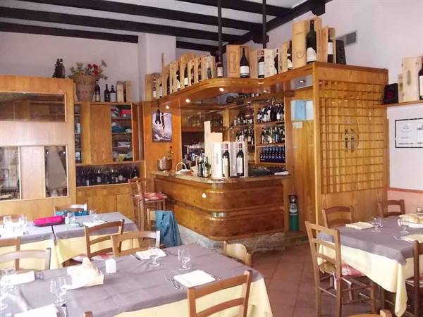 Trattoria dining room with set tables, wooden counter and wine bottles