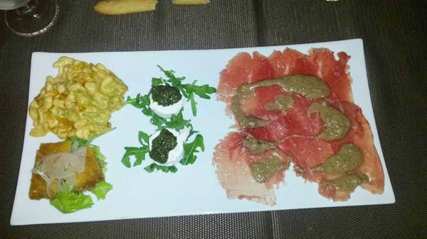 White plate with beef carpaccio, pesto mozzarella and fried bite on dark table