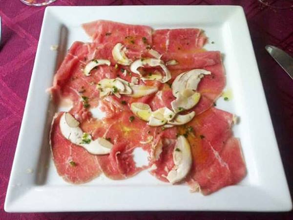 Raw beef carpaccio with mushrooms and oil on white square plate