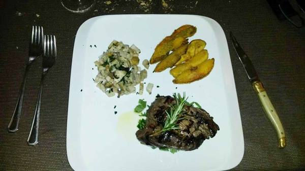 White plate with rosemary grilled steak, roasted potatoes and vegetables, cutlery beside