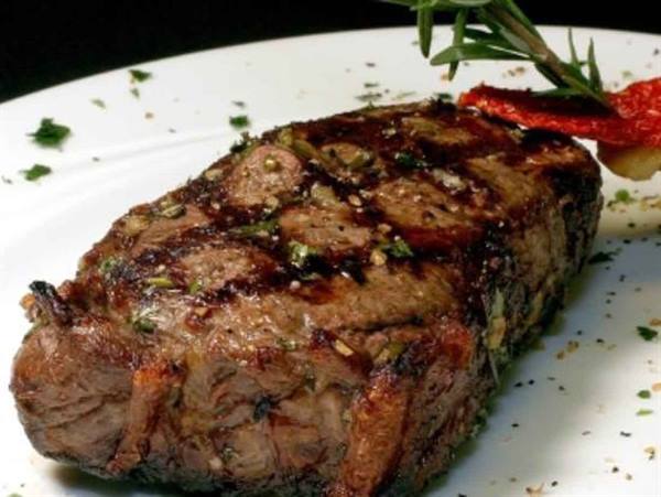 Grilled herb-seasoned steak on white plate, garnished with rosemary and sun-dried tomato