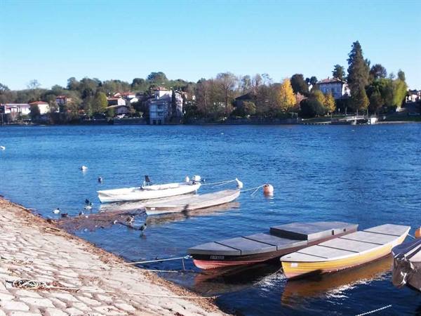 Rowboats moored by a pebble shore, blue water and a lakeside village
