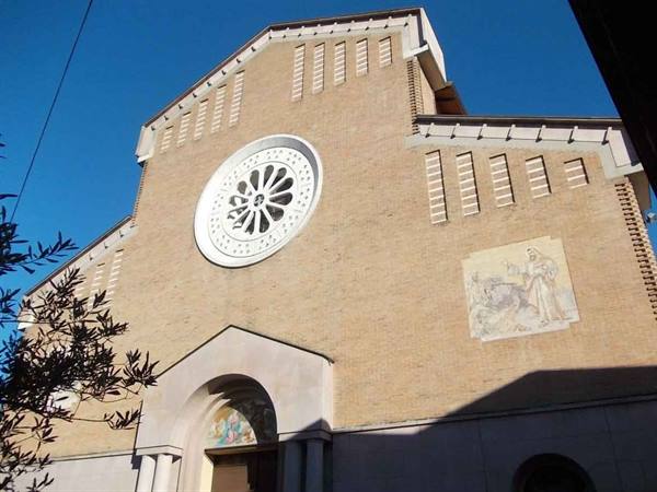 Brick church facade with white rose window and fresco, branches backlit