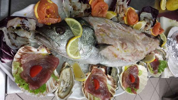Whole raw fish garnished with lemon on platter, surrounded by scallops and oysters