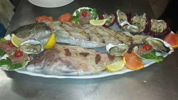 Grilled fish on large white platter with oysters, lemon slices and cherry tomatoes