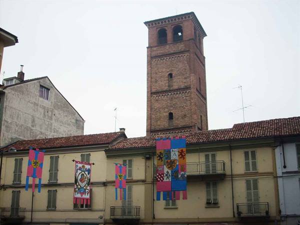 Medieval brick tower above buildings with colorful banners, grey sky