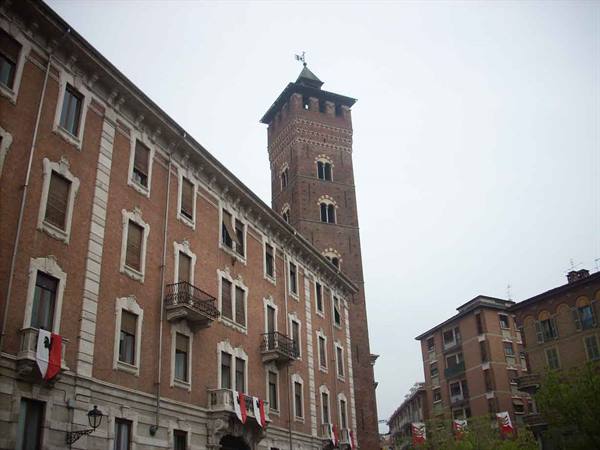 Brick medieval tower rising over flag-decorated buildings, Asti
