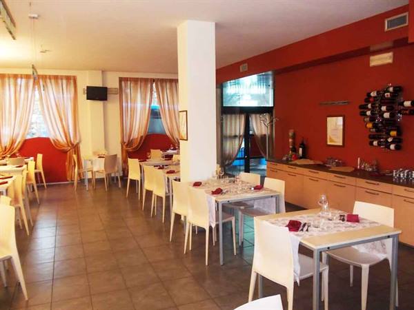 Restaurant dining room with set tables, white chairs, red walls and wine bottles