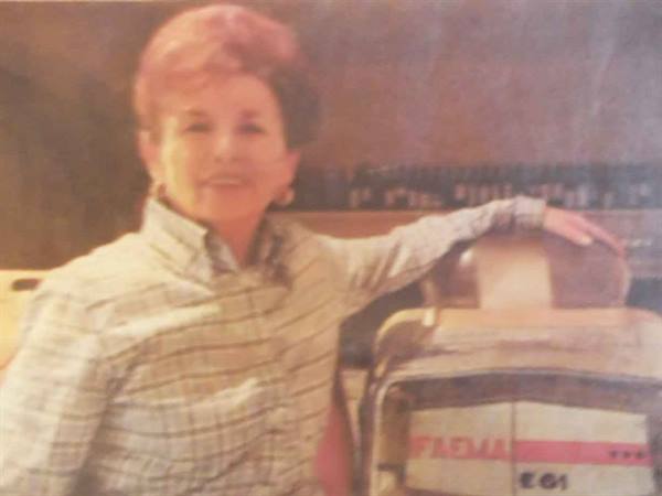 Smiling woman in checkered shirt leaning beside a Faema coffee machine, warm light