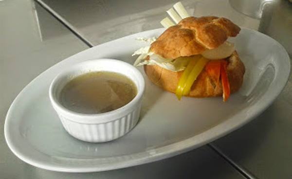 Stuffed sandwich with peppers and lettuce on white plate with sauce cup