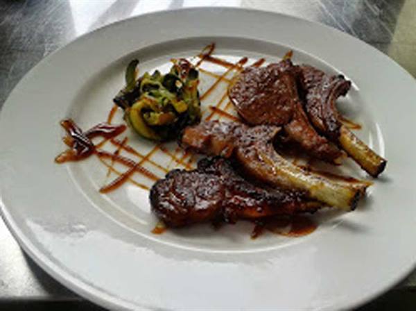 White plate with glazed lamb chops, sautéed zucchini and drizzled sauce