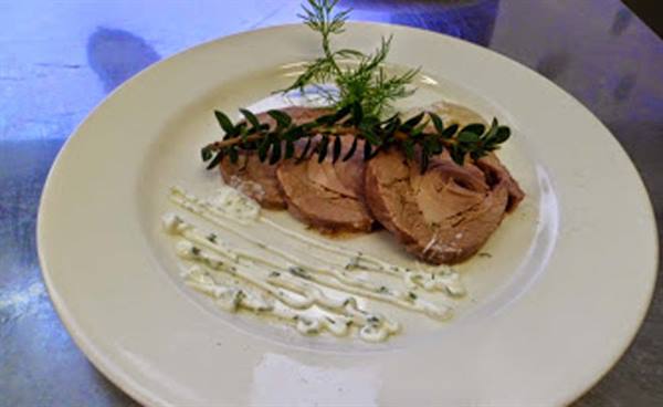 White plate with sliced veal tonnato, herb sauce and rosemary sprig