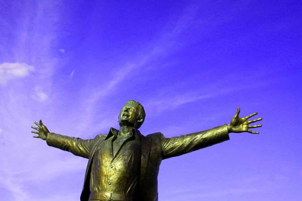 Bronze statue with outstretched arms against a blue sky