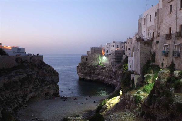 Polignano a Mare, white houses over cliffs and beach at dusk