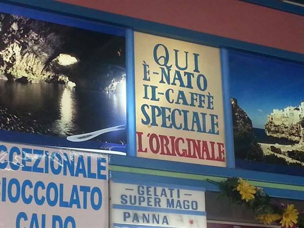 Sign reading 'Here the special coffee was born' beside grotto and village photos