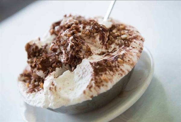 Cup of cream gelato with chocolate shavings and nuts, on marble table
