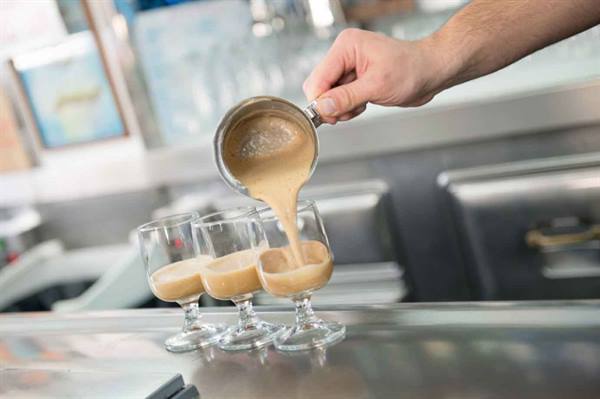 Barista pouring coffee cream into three small glass cups