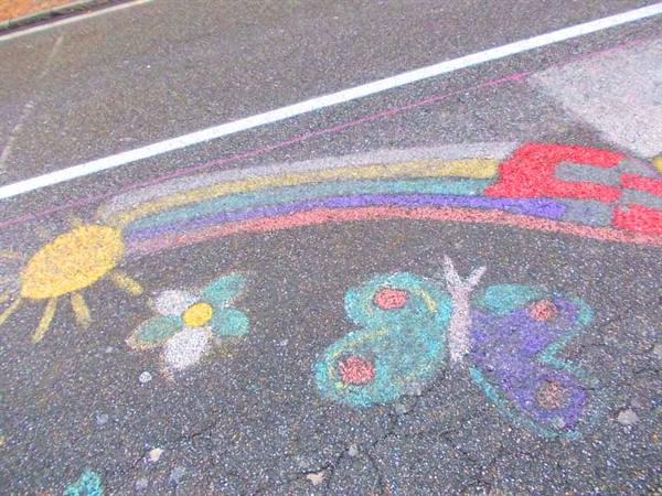 Chalk drawings on asphalt: sun, flower, butterfly and rainbow