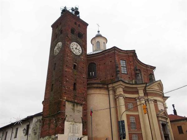 Brick clock tower beside baroque church, bells on top, grey sky